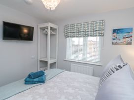 A bedroom with a bed folded towels on the bed a wall-mounted tv a small open closet with hangers a window with blinds and a patterned curtain at 48 Aysgarth Rise Bridlington
