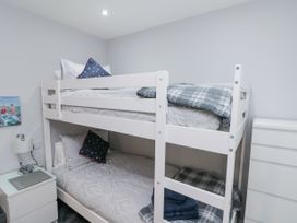 A bedroom with a white bunk bed with bedding pillows and blankets alongside a white nightstand and a chest of drawers at 48 Aysgarth Rise Bridlington