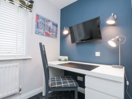 A desk with a chair in front of a blue wall with a wall-mounted television and two wall lamps a window with blinds a painting on the wall and a small toy bus on the desk at 48 Aysgarth Rise in Bridlington