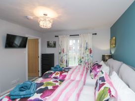 A bedroom with twin beds with colorful bedding a wall-mounted TV a black chest of drawers and floral curtains at 48 Aysgarth Rise in Bridlington