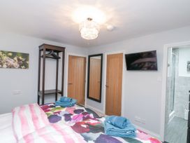 A bedroom with a bed, patterned bedding, folded towels, a wall-mounted TV, a mirror, wooden doors, a clothes rack, and an adjoining bathroom at 48 Aysgarth Rise Bridlington