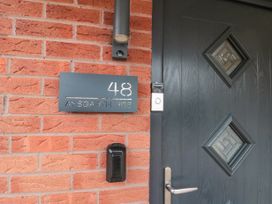 A black door with diamond-shaped windows a doorbell a house number plate with 48 aysgarth rise on a red brick wall at 48 Aysgarth Rise in Bridlington