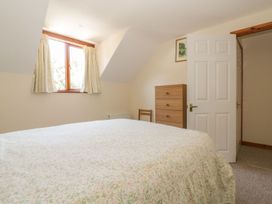 A bedroom with a bed, window, curtains, and a chest of drawers at Heron Cottage