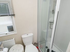 A bathroom with a toilet, a shower with glass doors, a wicker laundry basket, and a window with blinds at Ocean Pearl Kingsbridge
