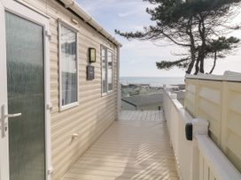 A pathway beside a beige mobile home with windows and a door overlooking a sea view with trees and rooftops at Ocean Pearl in Kingsbridge