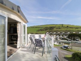 A balcony with chairs and a table overlooking green hills and houses at Ocean Pearl in Kingsbridge