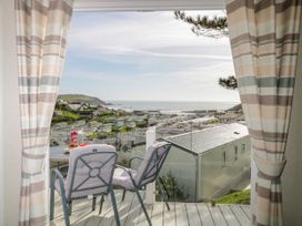 A balcony with two chairs and a table overlooking a holiday park with caravans and the sea beyond at Ocean Pearl in Kingsbridge
