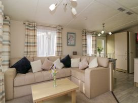 A living area with a beige sectional sofa with multiple cushions a wooden coffee table with flowers and a dining table with chairs in the background at Ocean Pearl Kingsbridge