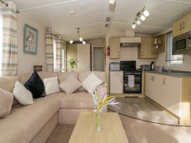 An open living space with a beige sectional sofa with pillows a wooden coffee table with flowers and a kitchen with wooden cabinets and appliances at Ocean Pearl in Kingsbridge