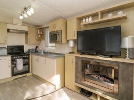 A kitchen with oven sink microwave and cabinets next to a living area with a TV lamps and electric fireplace at Ocean Pearl in Kingsbridge