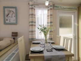 A dining table set with plates wine glasses and a vase of flowers near a window with striped curtains at Ocean Pearl in Kingsbridge