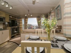 A dining table set with plates glasses and cutlery in a living area with a sofa a television and a window showing outdoor chairs and a sea view at Ocean Pearl in Kingsbridge