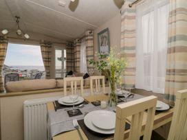 A dining table set with plates glasses and cutlery in a room with striped curtains and a view of the sea at Ocean Pearl in Kingsbridge