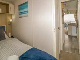 A bedroom with a bed and wall art leading to a hallway with a view of a living area and the sea at Ocean Pearl in Kingsbridge