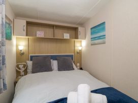 A bedroom with a double bed with white bedding and two gray pillows with wall lamps and wall art at Ocean Pearl in Kingsbridge