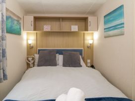 A bedroom with a double bed with grey pillows wall lights and ocean-themed paintings at Ocean Pearl in Kingsbridge