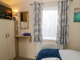 A bedroom corner with a wardrobe a wall-mounted TV a small shelf with a lamp and a decorative heart and a window with patterned curtains at Ocean Pearl in Kingsbridge