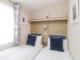 A bedroom with two single beds with blue cushions and a shelf with decorations above the beds at Ocean Pearl in Kingsbridge