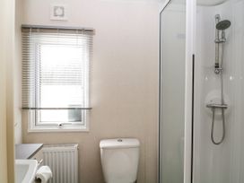 A bathroom with a toilet a shower area a window with blinds and a toilet paper holder at Ocean Pearl in Kingsbridge