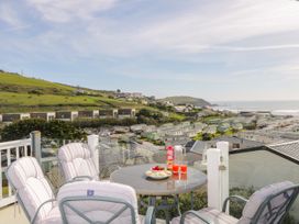 A balcony with a round table and cushioned chairs overlooking a holiday park and grassy hillside at Ocean Pearl in Kingsbridge