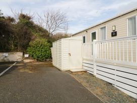 A mobile home with white railing and storage shed next to a parking area with bushes in the background at Ocean Pearl in Kingsbridge