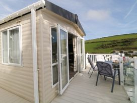 An outdoor patio with cushioned chairs and a table outside a cream-colored mobile home with glass doors at Ocean Pearl in Kingsbridge