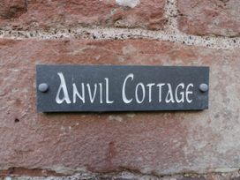 A slate sign with the text Anvil Cottage mounted on a stone wall at Anvil Cottage in Gatcombe near Blakeney