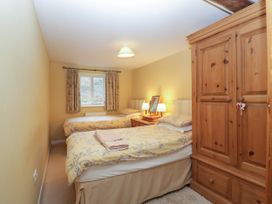 A bedroom with two single beds a wooden wardrobe a bedside table with lamps and a window at Anvil Cottage in Gatcombe near Blakeney