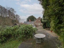 An outdoor patio area with a round table and four chairs surrounded by trees and bushes near a stone house at Anvil Cottage in Gatcombe near Blakeney