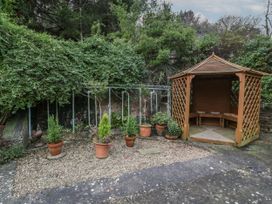 An outdoor area with a wooden gazebo surrounded by potted plants and greenery at Anvil Cottage in Gatcombe near Blakeney