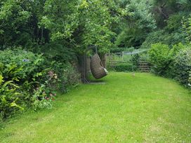 A garden with a hanging wicker chair and a rotary clothesline surrounded by trees and shrubs at Anvil Cottage in Gatcombe near Blakeney