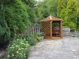 A garden area with a wooden gazebo surrounded by plants and trees at Anvil Cottage in Gatcombe near Blakeney