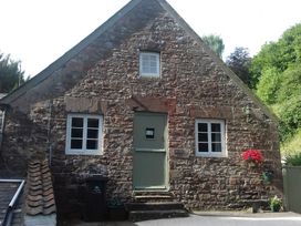 A stone cottage with a green door and two windows with white frames at Anvil Cottage in Gatcombe near Blakeney