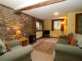 A living room with stone wall a small stove two green sofas and a patterned rug at Anvil Cottage in Gatcombe near Blakeney