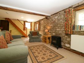 A living room with stone walls green sofa and armchair wooden staircase and patterned curtains at Anvil Cottage in Gatcombe near Blakeney