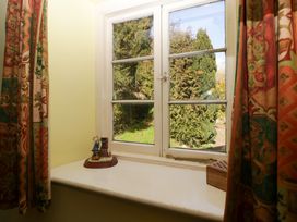 A window with patterned curtains and small decorative items on the windowsill at Anvil Cottage in Gatcombe near Blakeney