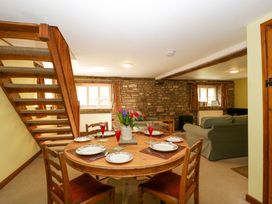 A dining area with a round wooden table set for six and a living room with sofas and a stone wall at Anvil Cottage in Gatcombe near Blakeney