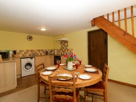 A kitchen and dining area with a round wooden table set for six under wooden stairs at Anvil Cottage in Gatcombe near Blakeney