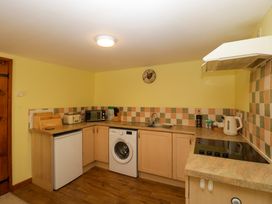 A kitchen with wooden cabinets a washing machine a small refrigerator a microwave toaster kettle and a stove at Anvil Cottage in Gatcombe near Blakeney