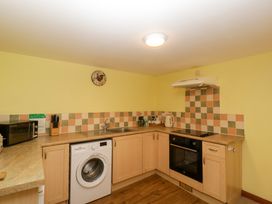 A kitchen with wooden cabinets microwave washing machine stove and kettle at Anvil Cottage in Gatcombe near Blakeney