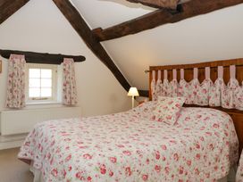 A bedroom with floral bedding wooden beams and a window at Anvil Cottage in Gatcombe near Blakeney