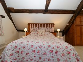 A bedroom with a floral bedspread on a double bed with wooden headboard and exposed wooden beams at Anvil Cottage in Gatcombe near Blakeney