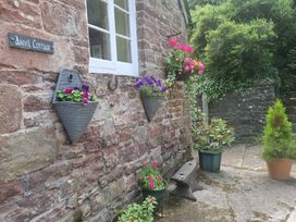 A garden with hanging planters and a stone wall at Anvil Cottage in Gatcombe near Blakeney