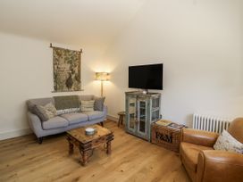 A living room with a sofa, armchair, TV, and coffee table at The Little Loft in Burford
