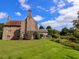 A stone house with chimneys and a large green lawn with trees at New Hall in Chirk