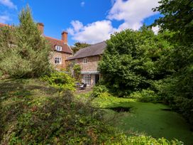 A stone house with a patio and chairs surrounded by trees and a pond covered with green vegetation at New Hall in Chirk