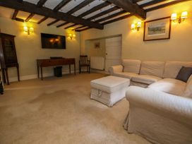 A living room with a beige sofa and ottoman a wooden cabinet a chair a TV on the wall and exposed ceiling beams at New Hall in Chirk