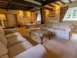 A living room with sofas a floral ottoman wooden ceiling beams and windows with floral curtains at New Hall in Chirk