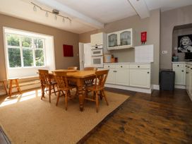 A kitchen with wooden table and chairs near a large window and white cabinets at New Hall in Chirk