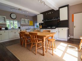 A kitchen with wooden dining table and chairs white cabinets and a clock on the wall at New Hall in Chirk